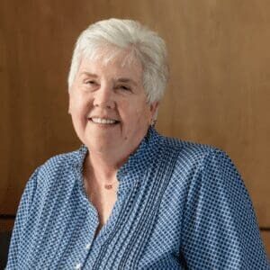 Smiling older woman in blue patterned blouse.