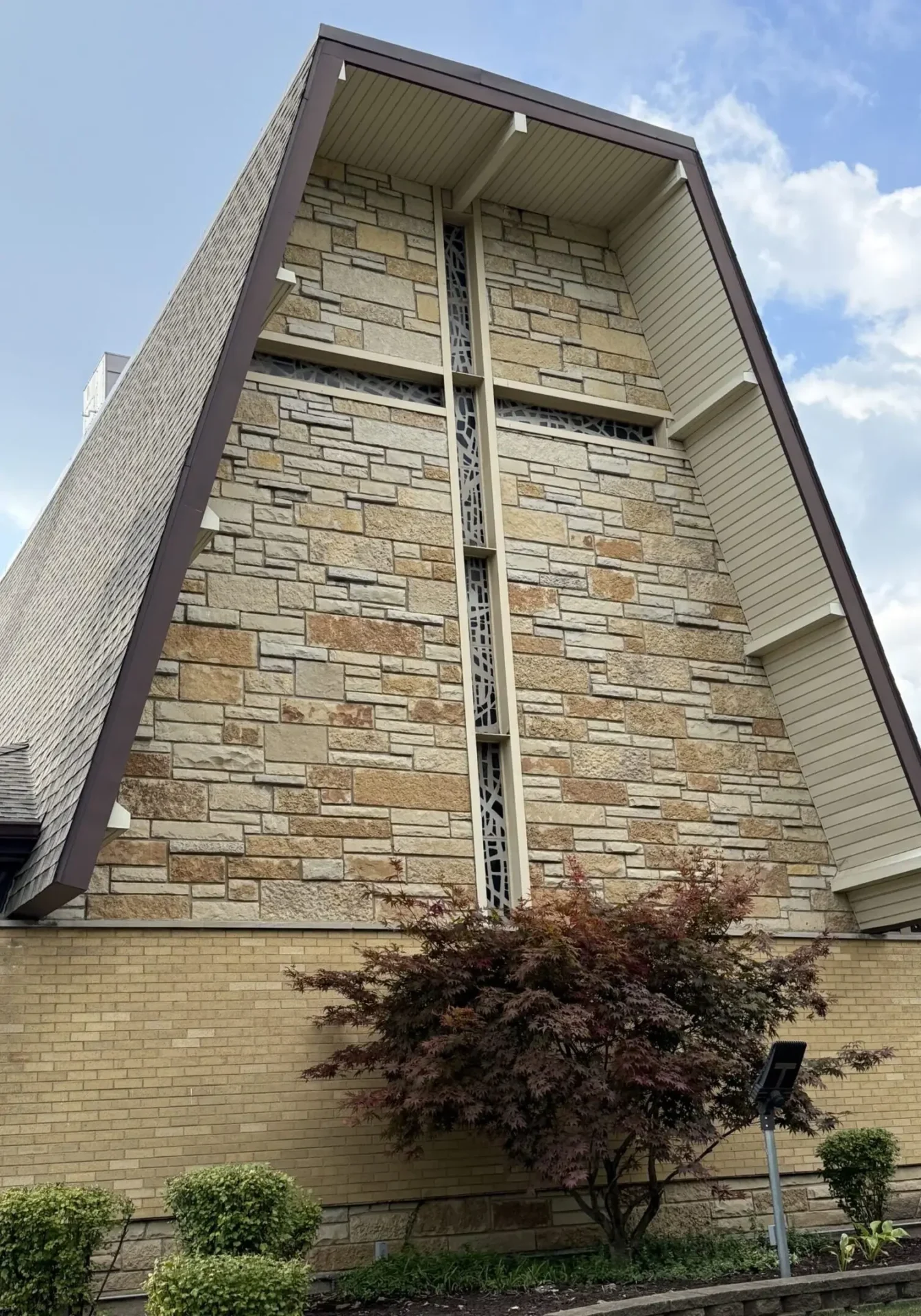 A tall building facade with stone and brick, featuring a vertical white cross.